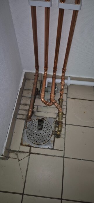 Kopparrör och golvbrunn i ett hörn av ett rum, med avslutade rörinstallationer och gjuten golvbrunn.