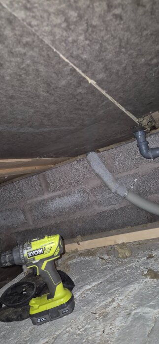 Underifrån ett golv med borr, ventilationsrör och grå betongvägg, sett i ett bygg- eller renoveringssammanhang.