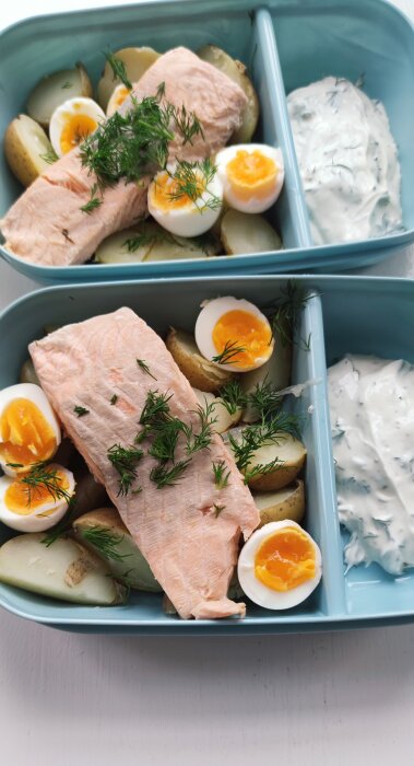 Tallrik med lax, kokta ägg, potatis och dill, serverat med en krämig sås i ett blått fackindelat fat.