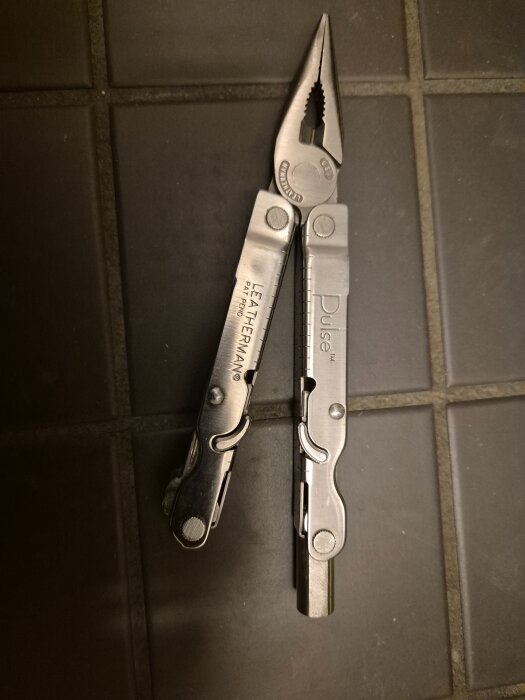 Multiverktyg Leatherman Pulse isärtagen, med viktiga verktyg och en egen tillverkad bitshållare. Ligger på ett klinkergolv.