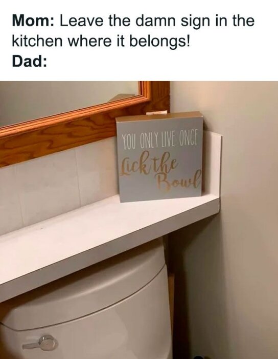 En bild av en skylt på en toalett med texten "You Only Live Once, Lick the Bowl" placerad ovanpå en vit cistern.
