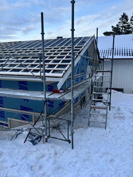 Bygge i vinterlandskap med ställning och snötäckt mark, där panel och tak uppförs på ett hus i kyla.