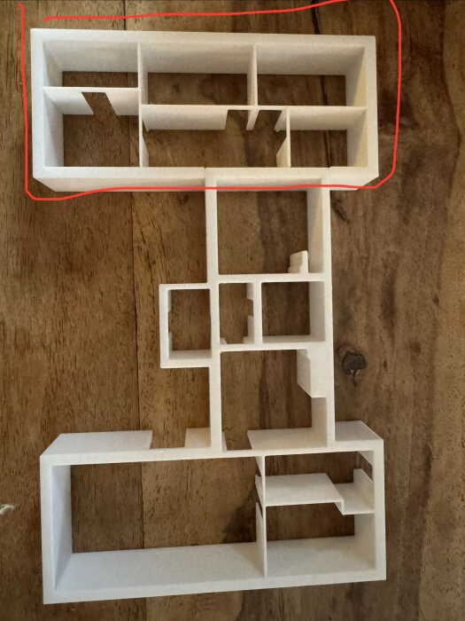 3D-modell av en byggnadsplan i vitt material på ett bord av trä, markerad med en röd linje upptill.