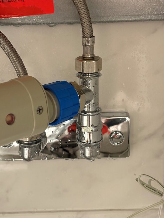 Närbild av ett rörsystem under en diskbänk med flexibla anslutningar och ventilkopplingar. Detaljer som vattenkopplingar syns tydligt.
