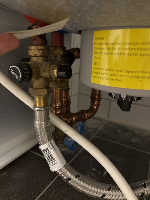 Ventil på ett Nibe-värmepumpssystem med koppar- och vattenrör, temperaturkontroll och varningsetikett.