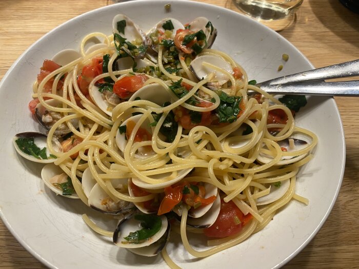 Tallrik med spaghetti vongole, innehållande pasta, musslor, tomater och persilja.