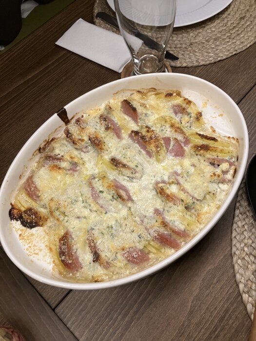 Ugnsform med gratäng på potatis och falukorv, täckt med ricotta, grädde, vitlök, persilja och västerbottenost, serverad på träbord.