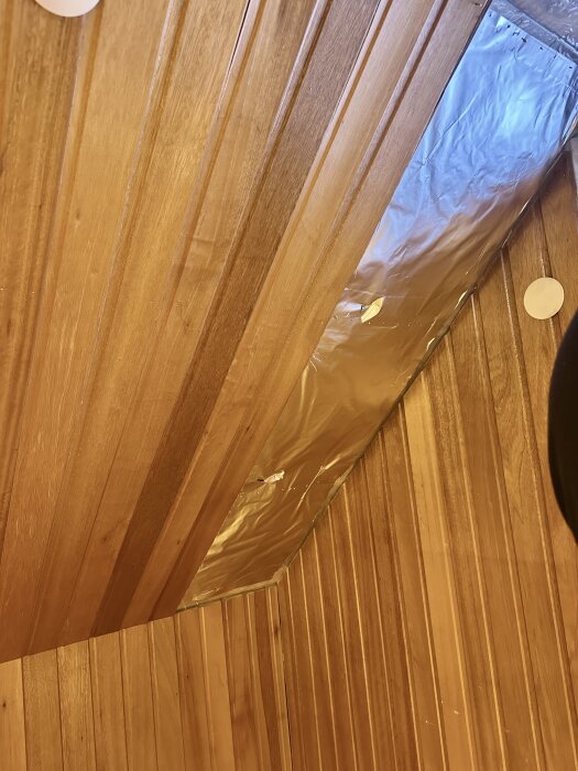 Träpanel på vägg med delvis synlig aluminiumfolie bakom, vid en renovering av ett rum på översta våningen.