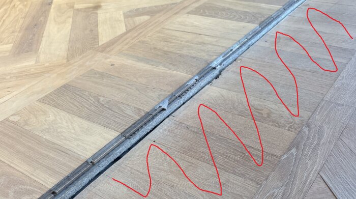 A section of a wooden floor with planks removed, red zigzag lines on the right indicating changes, possibly related to guide and leveling process.