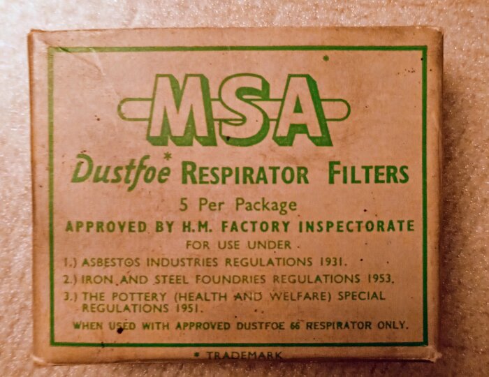 Filter från en MSA skyddsmask från 1950-talet, förpackat i en kartong med text om användning i asbest-, stål- och keramikindustrier.