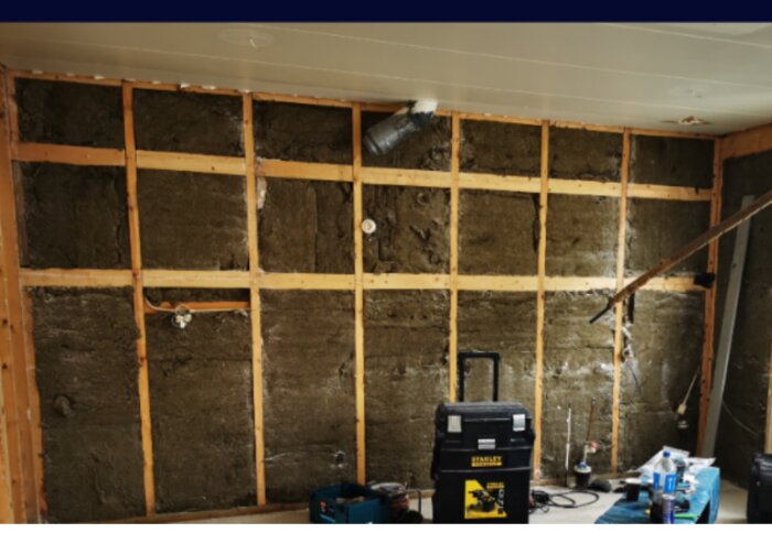Vägg med synlig isolering och träreglar, verktyg och verktygslåda framför, under renovering av ett hus byggt 1975 och renoverat 2021.