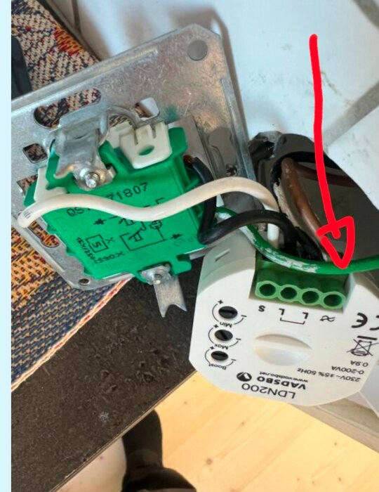 Grön ledare vid en Vadsbo LDN200 dimmer; inställningsknappar synliga och en röd pil pekar på anslutningspunkt.