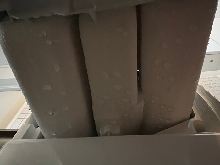 Närbild av insidan av en tvättmaskinsdoseringsfack med kondensdroppar synliga på ytan.