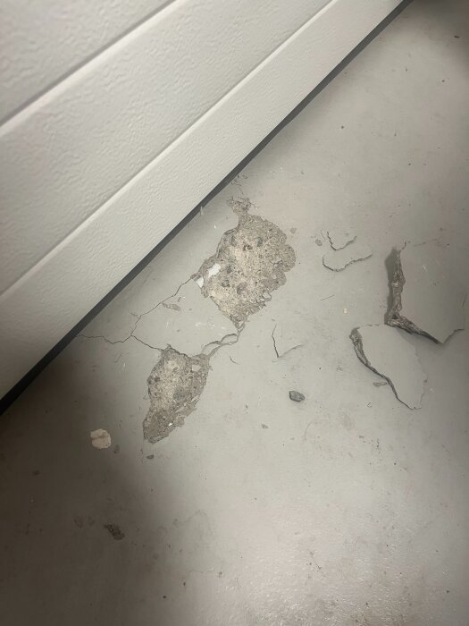 Sprucken betonggolvyta med synligt slitage och skavanker intill en vit vägg eller struktur.