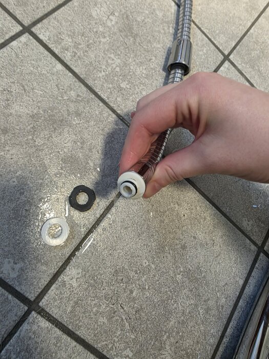 Hand monterar en vattenslang med packningar på ett kaklat golv.