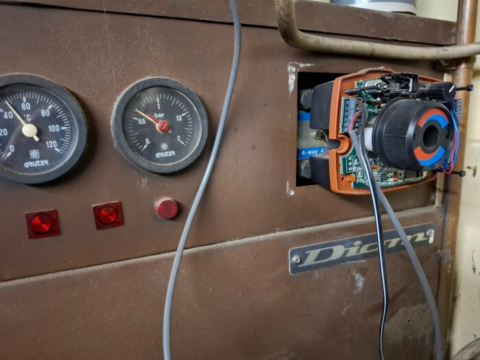 Närbild av en Diom vedpanna med två manometrar och en delvis isärplockad elektronisk komponent.