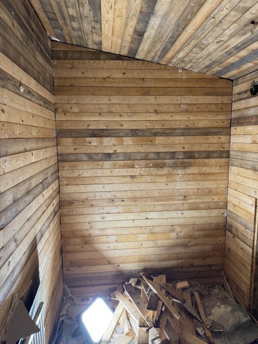 Väggar med träpanel i ett badrum under renovering, med en ljuskälla och en hög brädor på golvet.