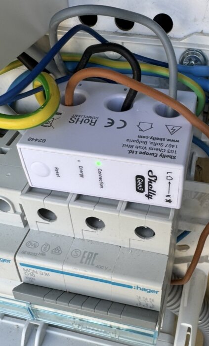 En Shelly enhet installerad i elcentral med flera anslutna kablar och lysande indikator för anslutning i en trång installation.