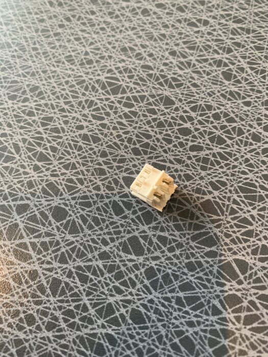 En vit kontakt för kablar till en Bosch-diskmaskin ligger på ett bord med geometriskt mönster.