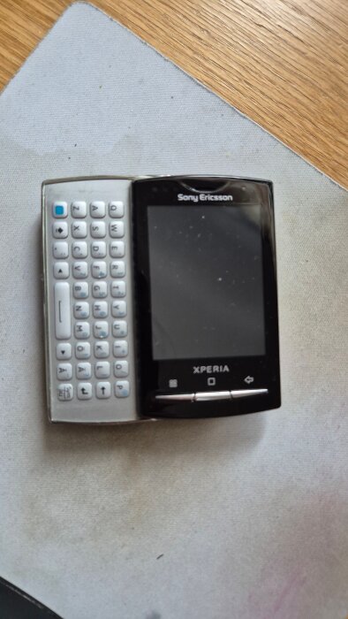 Gammal Sony Ericsson-mobiltelefon med utdragbart tangentbord, saknar stativ.