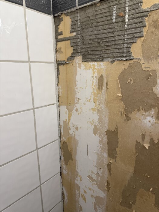 Vägg med delvis borttaget kakel och exponerat gips, visar renoveringsbehov i badrum innan ny kakling.