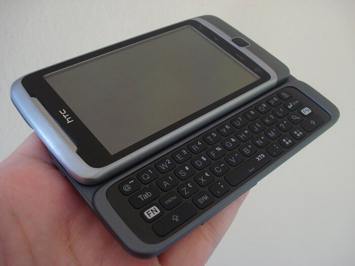 HTC smartphone med utskjutbart tangentbord hålls i handen, modell med grå ram och svart tangentbord.