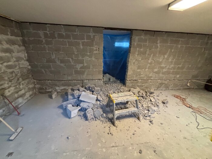 En hjärtvägg med ett nyupptaget hål och bråte vid basen, en blå presenning i bakgrunden och en stege framför.