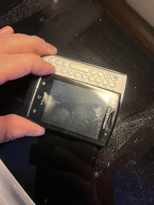 Gammal Sony Ericsson-mobiltelefon med utfällbart tangentbord visas, hålls av en hand, användes i diskussion om lyxmobiltelefoner.