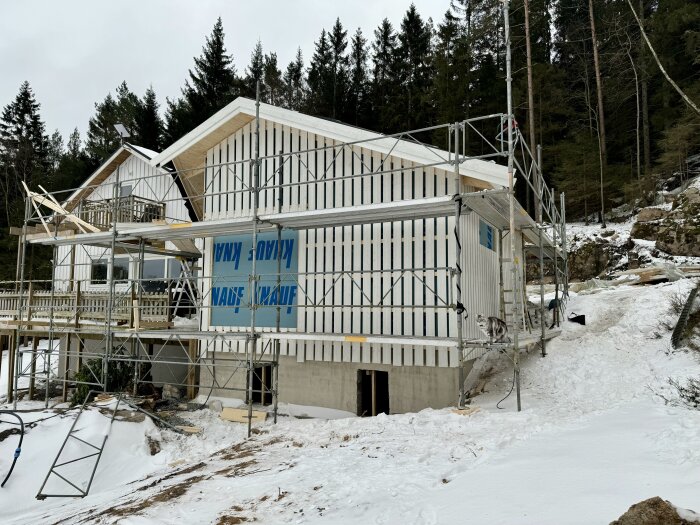 En byggarbetsplats med ett hus under konstruktion, täckt av snö med byggnadsställningar runt omkring.