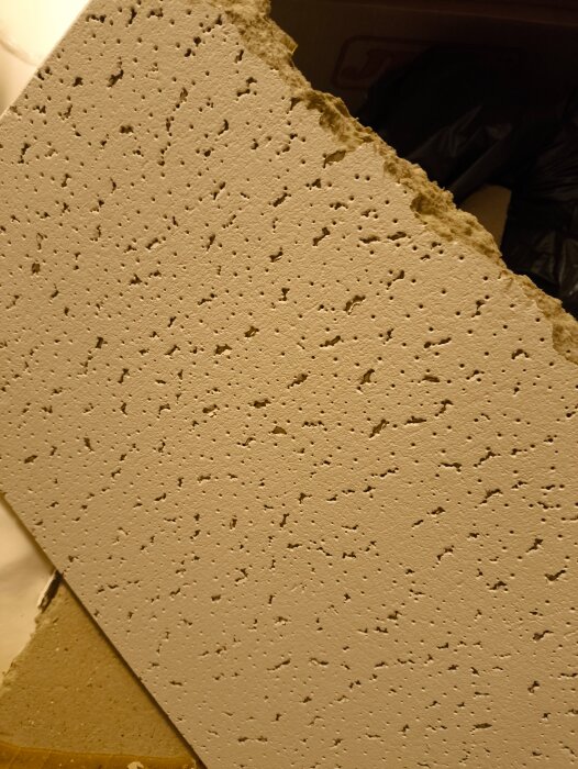 Bruten akustikplatta med perforerad yta, osäkerhet kring material, asbest eller mineralull, från källartak.