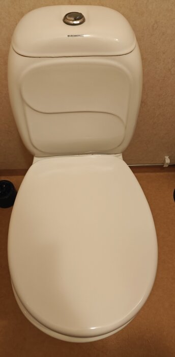 Vit toalettstol av märket Svedbergs, cirka 20 år gammal, mot en beige bakgrund.
