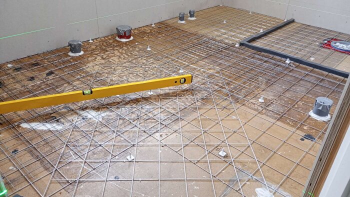 Badrumsgolv med armeringsnät på plywood och gips, här syns en gul vattenpass, redo för spackling och mattläggning.