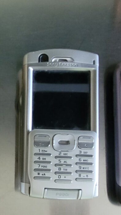 Ericsson P990i mobiltelefon med många knappar, beskriven som buggig och opraktisk.