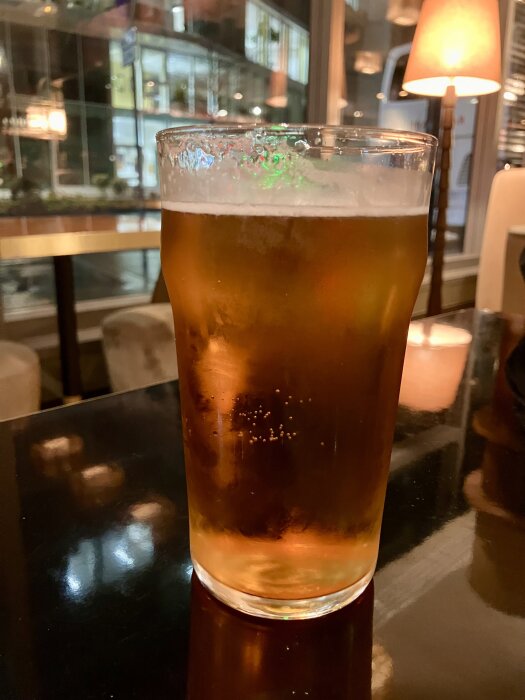Ett glas med belgisk fatöl, på ett bord med spegelblank yta och dämpad belysning i bakgrunden.