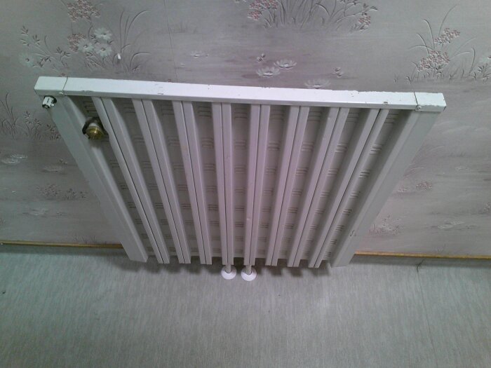 Vitt panelradiator med grova vertikala sektioner, monterat på en väg med blommigt mönster i ett 1970-talshus.