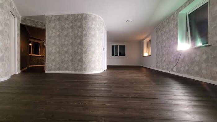 Rum med mörkt trägolv installerat, ljus blommig tapet och stora fönster. Golvet är Dala-Floda HardPine Onyx 21mm med golvvärme.