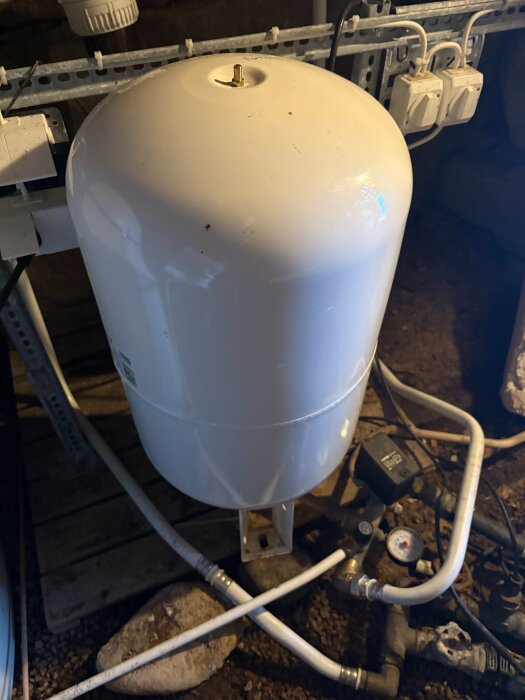 Vit trycktank och rör kopplade till en mätare i en källare.