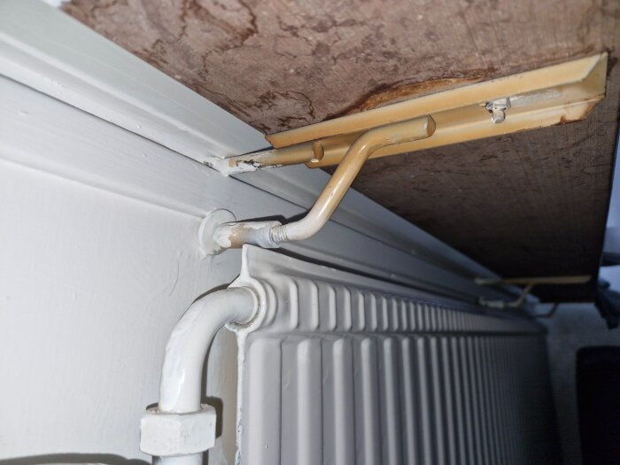 Undersida av fönsterbräda med metallbeslag ovanför ett element.