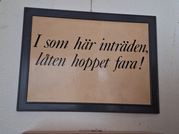 Inramad tavla med texten "I som här inträden, låten hoppet fara!" hängande på en vägg.