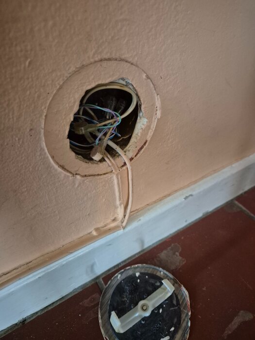Ett öppnat eluttag i väggen med synliga kablar samt ett avlägsnat lock ligger på golvet.