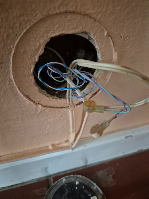 Öppen väggcirkel i hall med lösa kablar som sticker ut, kabelstrumpor syns. Kablarna går in i väggen, synlig röra av småkablar.