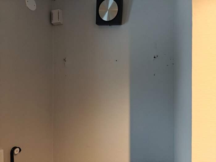 Vägg med flera hål och märken där en hatthylla tidigare satt; väggens yta är strukturerad i en svagt blågrå färg.