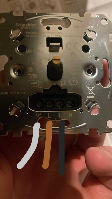 Närbild av en Schneider Electric elkomponent med kontaktterminaler, märkningar och färgkodade kablar i närheten, hålls av en hand.