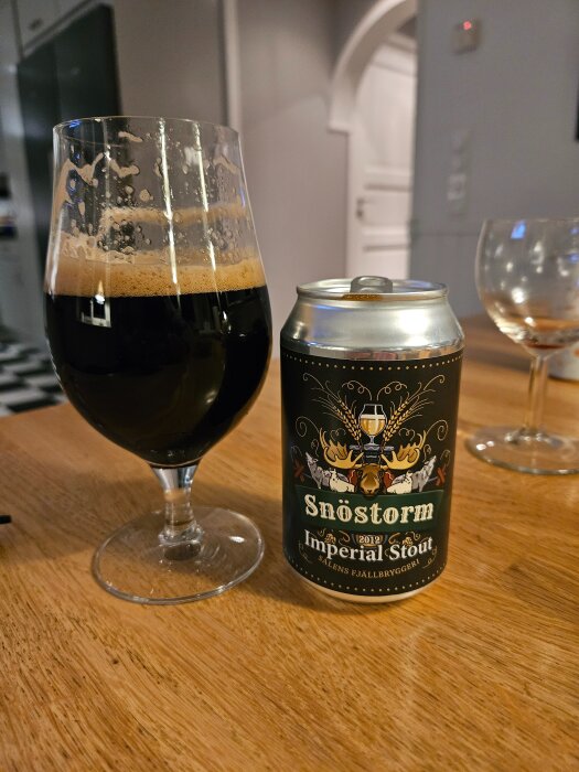 Ett glas och en burk Snöstorm Imperial Stout från Salens Fjällbryggeri på ett träbord.