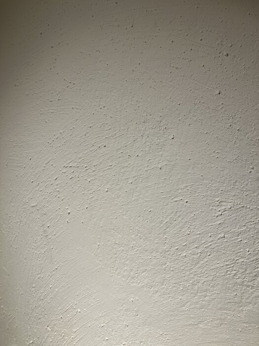 En grovt strukturad vägg med ojämn yta, behandlad med blandning av spackel, putsbruk och färg för att likna puts.