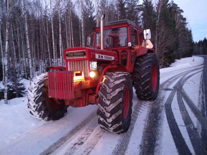 Röd BM-Volvo traktor på en snötäckt landsväg omgiven av träd.