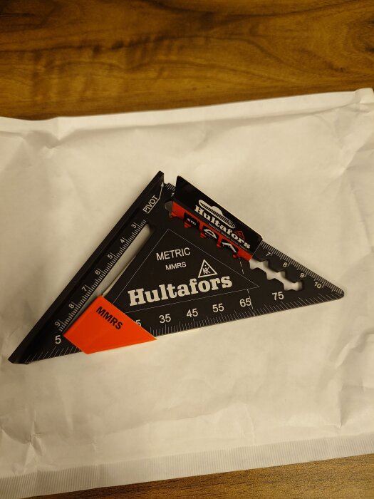 Triangulär vinkelmätare från Hultafors, modell MMRS, ligger på ett vitt papper på ett träbord.