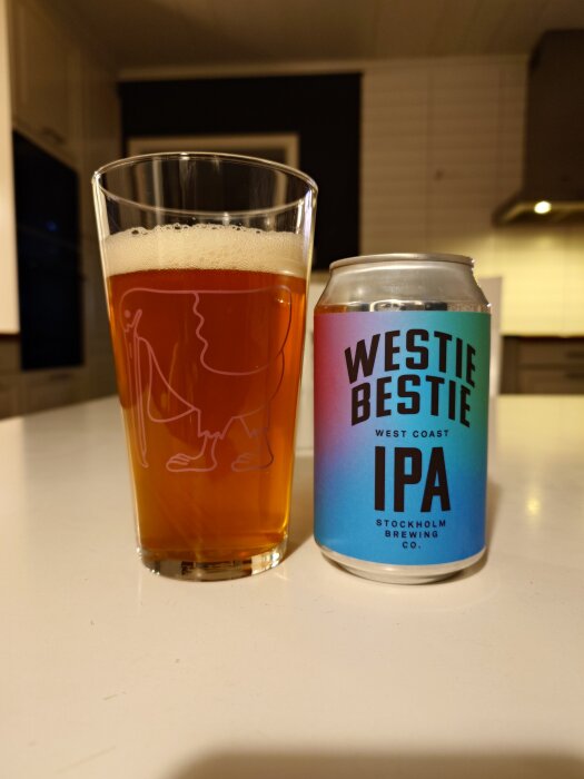 Glas med Westie Bestie IPA öl bredvid en burk på ett köksbord.