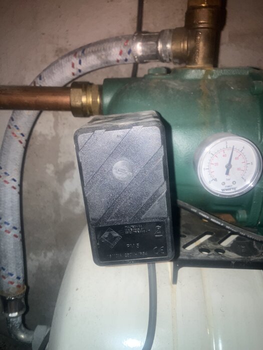 En svart Italienica PM 5-enhet monterad nära en mätare och en kopparledning med slang, sannolikt del av en vattenpumpinstallation.