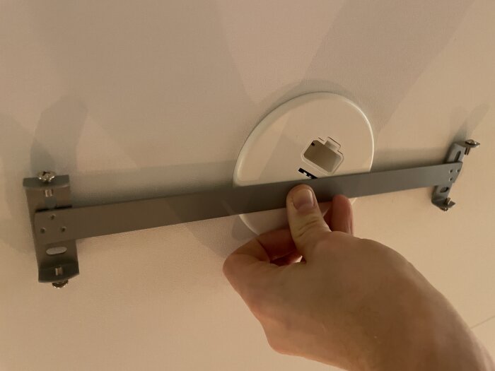 Hand håller metallfäste vid lamputtag i tak.